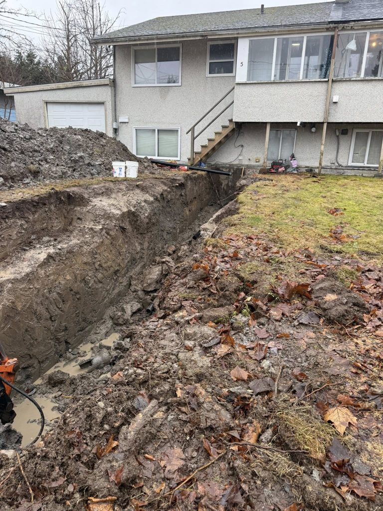 Excavated trench running alongside a house for drainage, utility, or foundation-related site work.