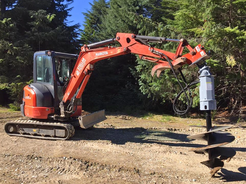 Orange excavator clearing brush and vegetation beside a residential property during land preparation work.