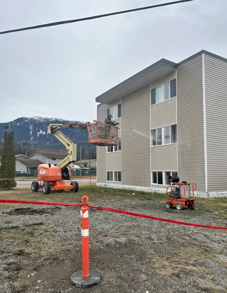 Worker pressure washing exterior of multi-storey building using boom lift