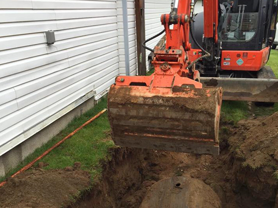 Excavator trenching beside house foundation utility install Kitimat